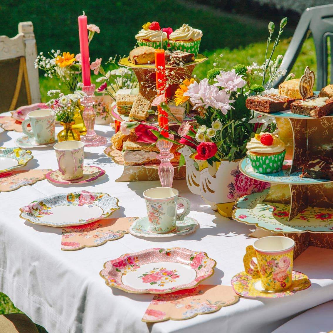 Decoratore vicino al tavolo da festa in colori pastello con tovaglia rosa,  piatti colorati di carta, tazze e posate dorate. decorazione festa di  compleanno ragazza, tappi festivi.